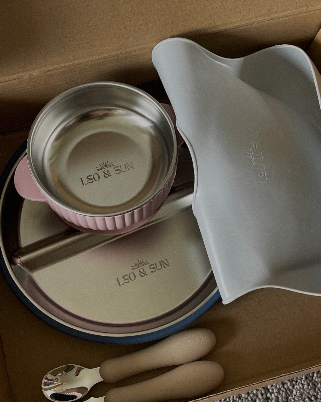 Children's tableware set with bowls, spoon, and fork on a cardboard surface