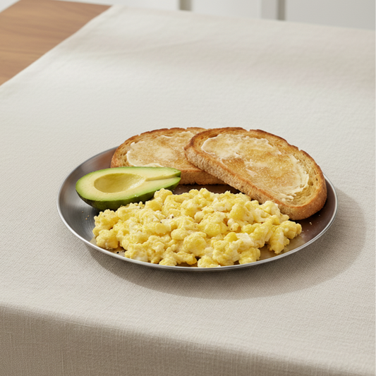 Plate of scrambled eggs, toast, and avocado on a beige tablecloth.